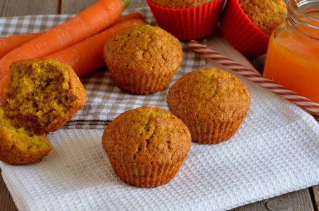 Muffin alle carote su tovaglietta bianca con carote e succo di frutta sullo sfondo