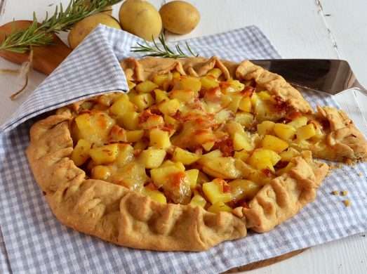 Torta salata con patate, speck e scamorza sutovaglietta a quadretti e tavolo bianco.