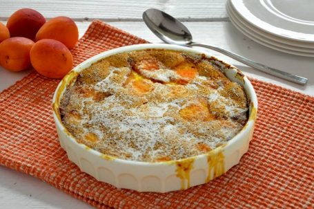 Teglia bianca rotonda con clafoutis alle albicocche su tovaglietta arancione