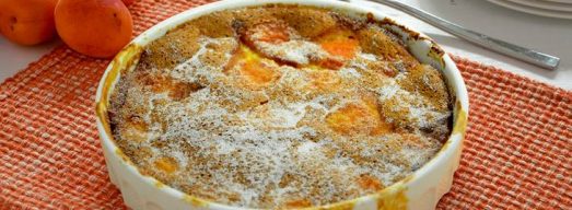 Teglia bianca rotonda con clafoutis alle albicocche su tovaglietta arancione