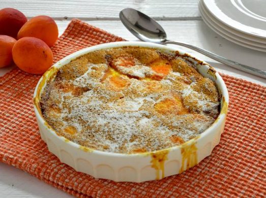 Teglia bianca rotonda con clafoutis alle albicocche su tovaglietta arancione
