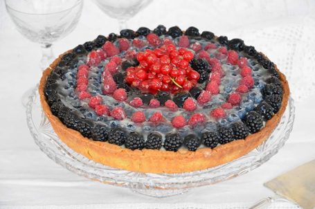 Alzatina di vetro con sopra la crostata ai frutti di bosco intera