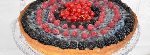 Alzatina di vetro con sopra la crostata ai frutti di bosco intera