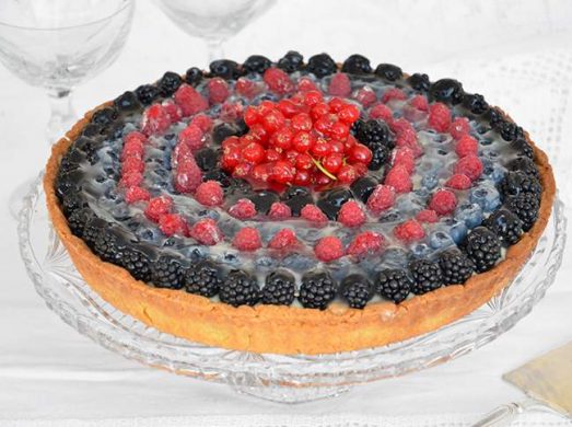 Alzatina di vetro con sopra la crostata ai frutti di bosco intera