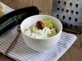 Ciotola bianca con crema tzatziki e cetriolo e grattugia sullo sfondo