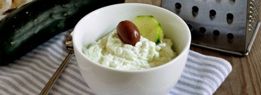 Ciotola bianca con crema tzatziki e cetriolo e grattugia sullo sfondo
