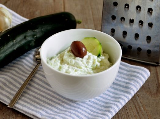 Ciotola bianca con crema tzatziki e cetriolo e grattugia sullo sfondo