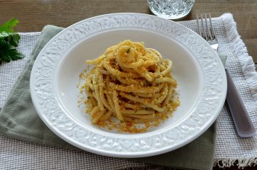 Piatto bianco con spaghetti con acchiughe e pangrattato su tavola apparecchiata