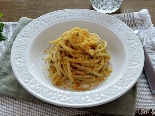 Piatto bianco con spaghetti con acchiughe e pangrattato su tavola apparecchiata