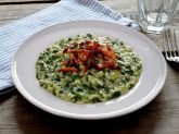 Piatto di risotto con spinaci e pancetta con tovaglietta celeste, forchetta e bicchiere