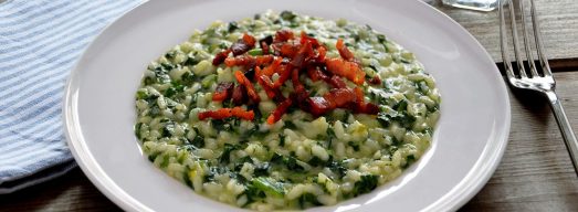 Piatto di risotto con spinaci e pancetta con tovaglietta celeste, forchetta e bicchiere