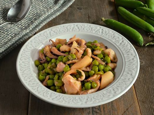 Piatto con seppie e piselli su tavola con baccelli e tovaglietta