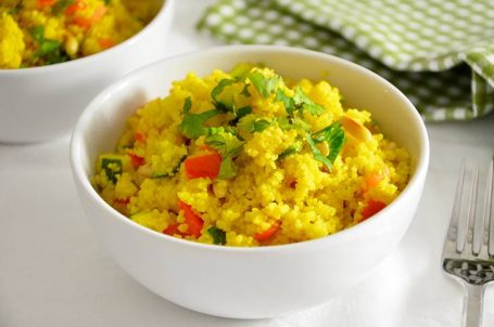 Ciotola di cous cous alle verdure saltate in primo piano con tavaglietta a quadretti verde e bianca