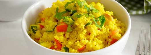 Ciotola di cous cous alle verdure saltate in primo piano con tavaglietta a quadretti verde e bianca
