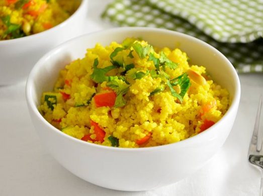 Ciotola di cous cous alle verdure saltate in primo piano con tavaglietta a quadretti verde e bianca