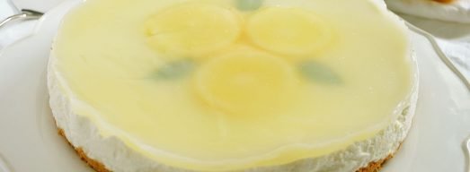 Cheesecake al limone intera su piatto bianco con limoni sullo sfondo