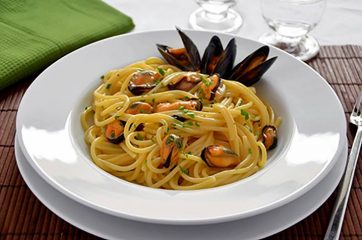 Piatto binaco con spaghetti con le cozze su tavola apparecchiata