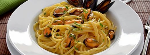 Piatto binaco con spaghetti con le cozze su tavola apparecchiata