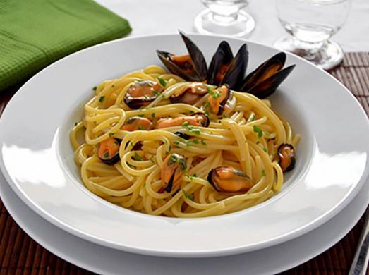 Piatto binaco con spaghetti con le cozze su tavola apparecchiata