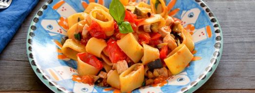 Piatto colorato con pasta con pesce spada e melanzane in primo piano