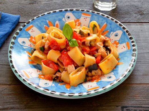 Piatto colorato con pasta con pesce spada e melanzane in primo piano