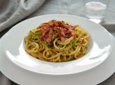 Piatto con pasta con zucchine e asparagi e prosciutto croccante su tavola apparecchiata