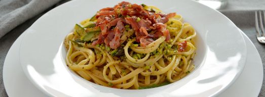 Piatto con pasta con zucchine e asparagi e prosciutto croccante su tavola apparecchiata