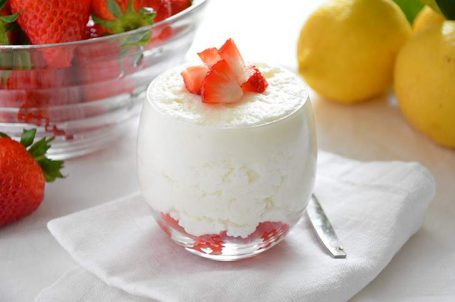 Bicchiere di mousse al limone con fragole fresche con limoni e fragole sullo sfondo