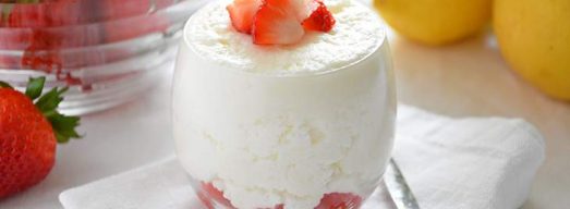 Bicchiere di mousse al limone con fragole fresche con limoni e fragole sullo sfondo