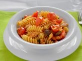 Piatto bianco con pasta con sgombro e pomorodini su tovaglia verde