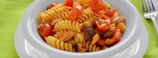 Piatto bianco con pasta con sgombro e pomorodini su tovaglia verde