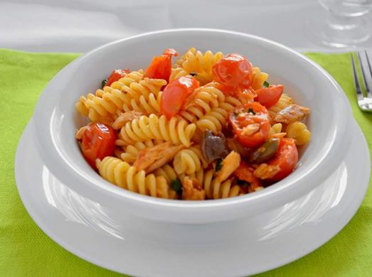 Piatto bianco con pasta con sgombro e pomorodini su tovaglia verde
