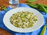 Piatto di risotto con i piselli su tovaglietta azzurra e baccelli sullo sfondo