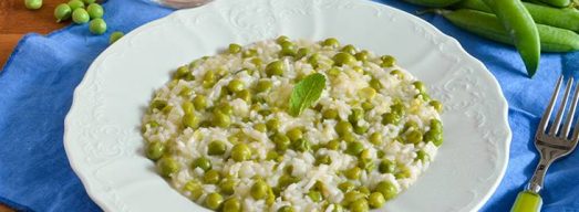 Piatto di risotto con i piselli su tovaglietta azzurra e baccelli sullo sfondo