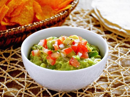 Ciotola bianca con Guacamole con nachos sullo sfondo
