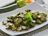 Piatto bianco con zucchine trifolate con zucchine crude sullo sfondo