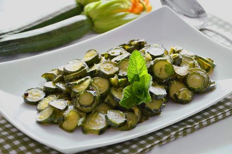 Piatto bianco con zucchine trifolate con zucchine crude sullo sfondo