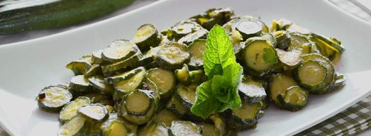 Piatto bianco con zucchine trifolate con zucchine crude sullo sfondo