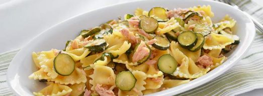Piatto ovale con farfalle con zucchine e tonno su tavola bianca
