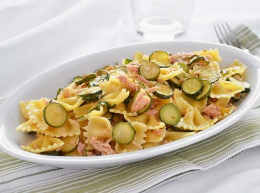 Piatto ovale con farfalle con zucchine e tonno su tavola bianca