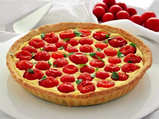 Piatto da portata con torta salata ricotta e pomodorini su tovaglia bianca