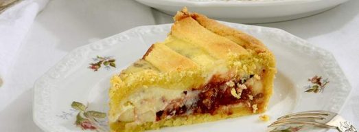 Piattino con fetta di crostata di ricotta e cioccolato e crostata sullo sfondo.