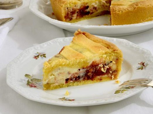 Piattino con fetta di crostata di ricotta e cioccolato e crostata sullo sfondo.