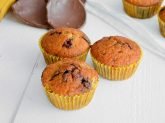Tre muffins in primo piano e altri con pezzi di cioccolato e banane sullo sfondo
