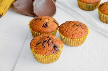 Tre muffins in primo piano e altri con pezzi di cioccolato e banane sullo sfondo
