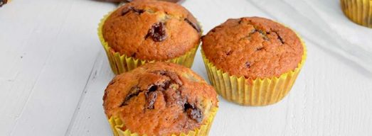 Tre muffins in primo piano e altri con pezzi di cioccolato e banane sullo sfondo