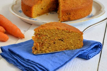 Fetta di torta di carote su tovagliolo blu con torta e carote sullo sfondo