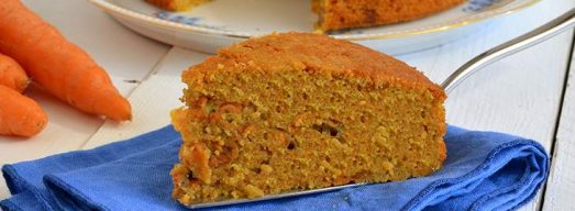 Fetta di torta di carote su tovagliolo blu con torta e carote sullo sfondo