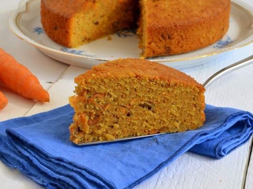 Fetta di torta di carote su tovagliolo blu con torta e carote sullo sfondo