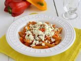 Piatto bianco con pasta con peperoni e feta su tovaglietta gialla